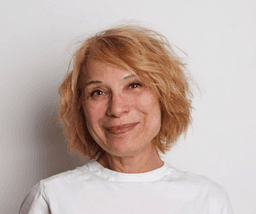 Portrait of Maria Rodriguez smiling gently against a lavender background